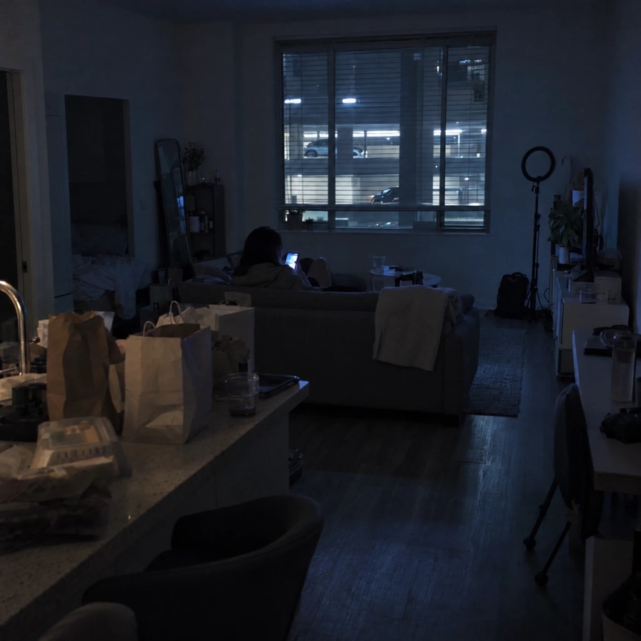 A person slumped on a grey sofa in a dim studio, lit by a phone.